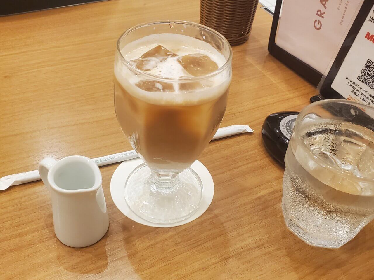 ッキーダック有楽町店で提供されたアイスミルクティー。グラスに入ったミルクティーとシロップの入ったピッチャーが木目のテーブルに置かれている
