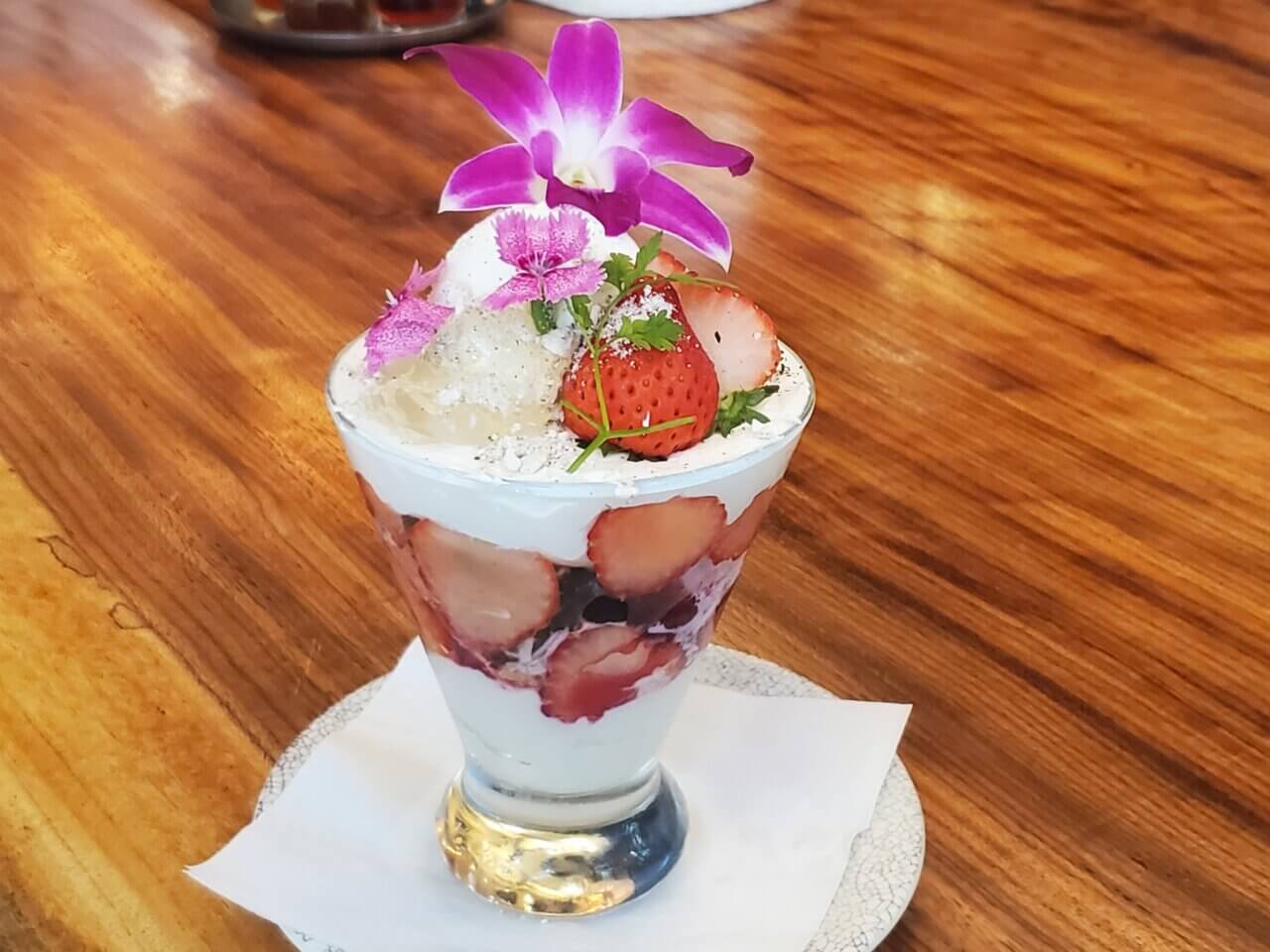 苺やタピオカを重ねたパフェにエディブルフラワーが飾られた華やかなデザートの写真。